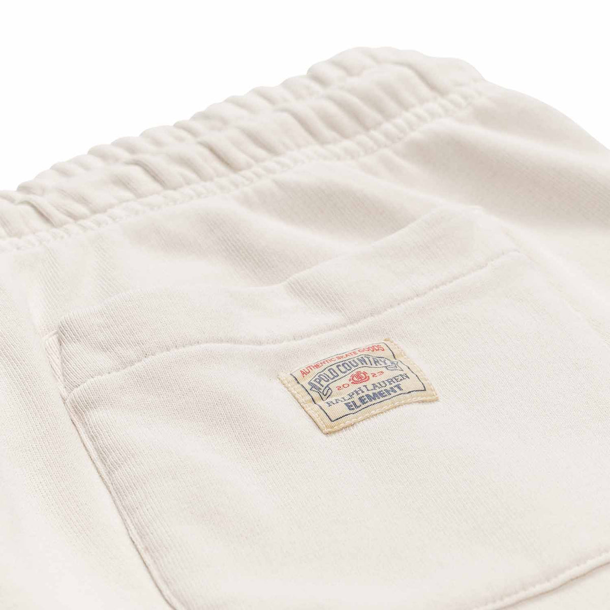 Polo Ralph Lauren x Element Sweatpants in cream with draw string and elastic in ankles. With back pocket on right side and small patch Polo Ralph Lauren x Element logo on pocket. Close up photo of patch with red and blue Polo Ralph Lauren x Element Logo.