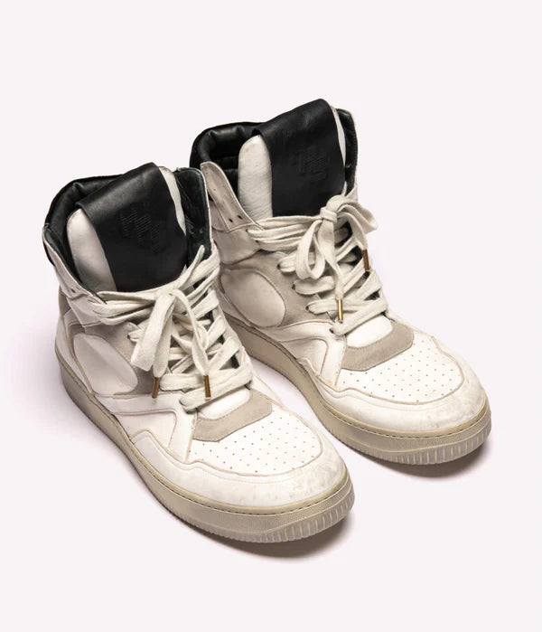 Human recreational services distressed white leather sneaker with black top leather detailing on tongue, white laces, and white sole. 
