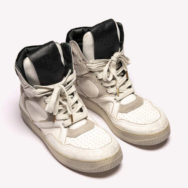 Human recreational services distressed white leather sneaker with black top leather detailing on tongue, white laces, and white sole. 