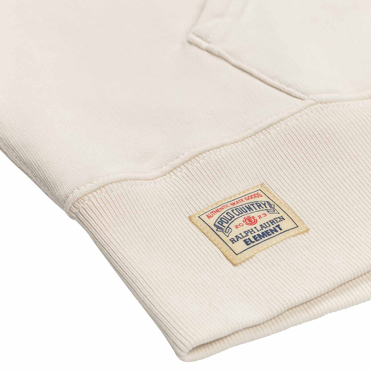 Polo Ralph Lauren x Element Skateboards Hoodie in cream white color. Detail shot of Small sewn on square logo at bottom left of hoodie on waist band. Light brown patch with red and blue writing.